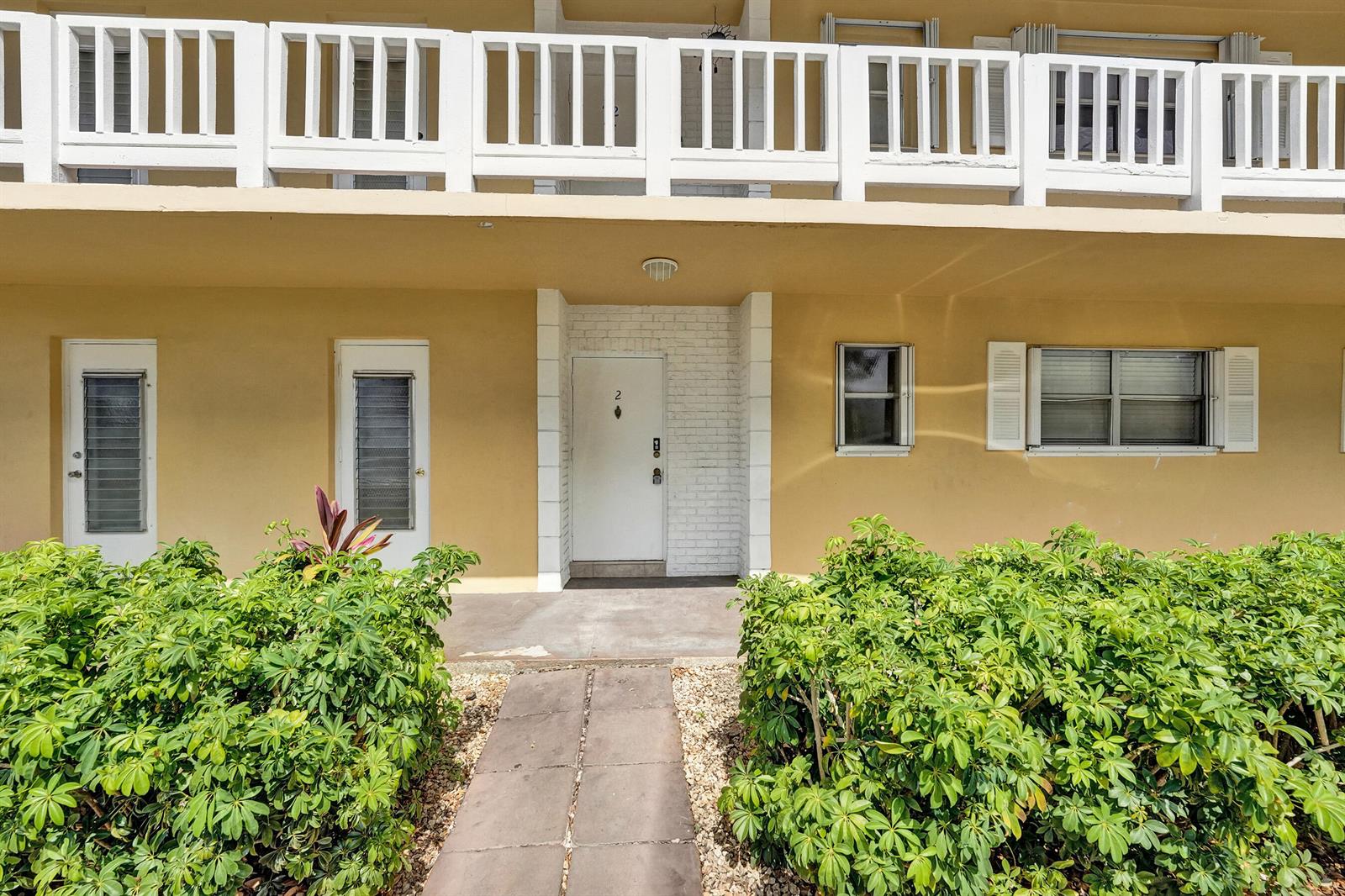The exterior of a tan building features a white front door, windows, and landscaping — 600 SE 2nd Avenue # K2, Deerfield Beach FL 33441, DEERFIELD BEACH, FL