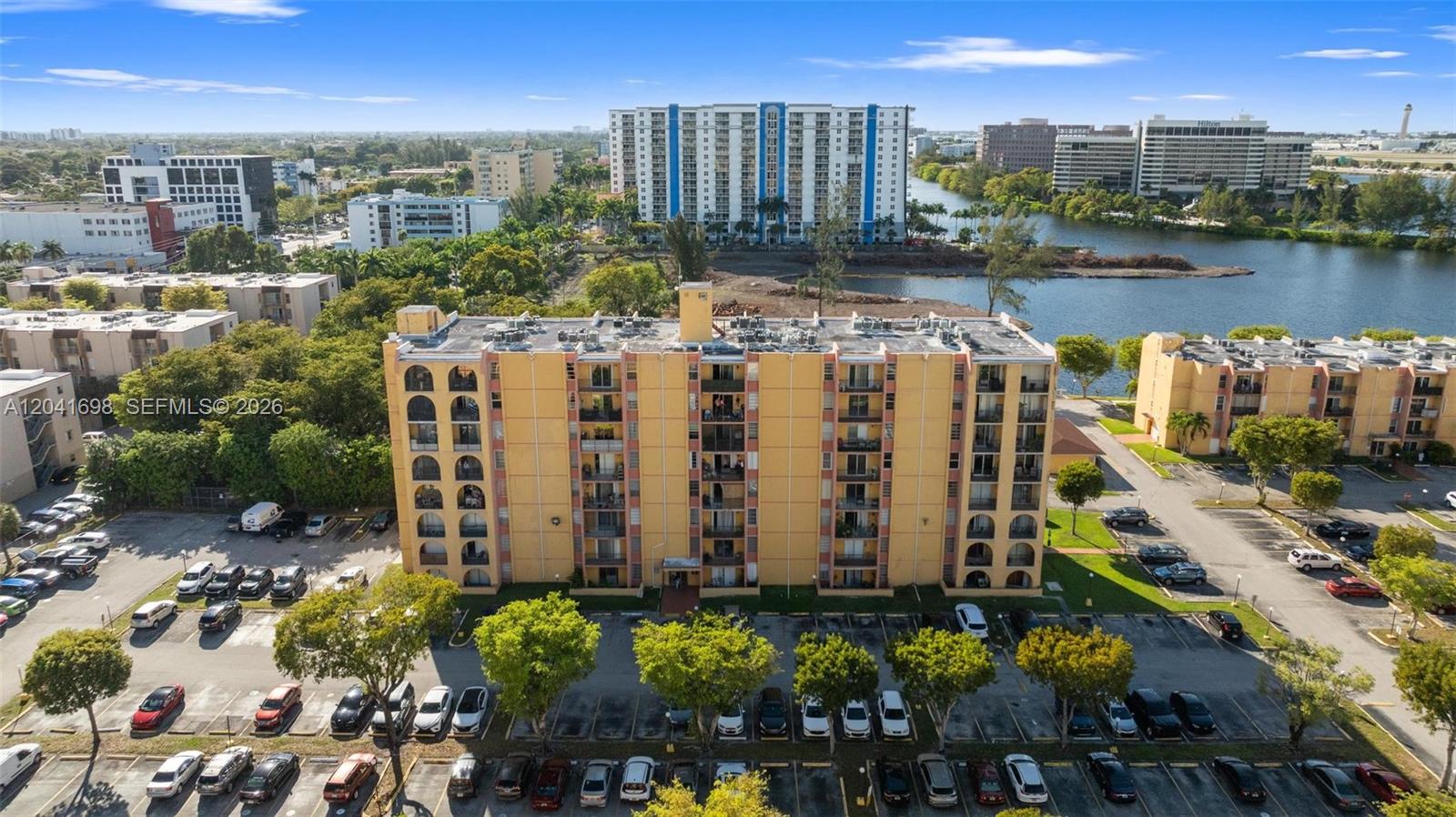 An aerial view shows a multi-story yellow apartment building with a parking lot and lake — 4801 NW 7th St # 16, Miami FL 33126, MIAMI, FL