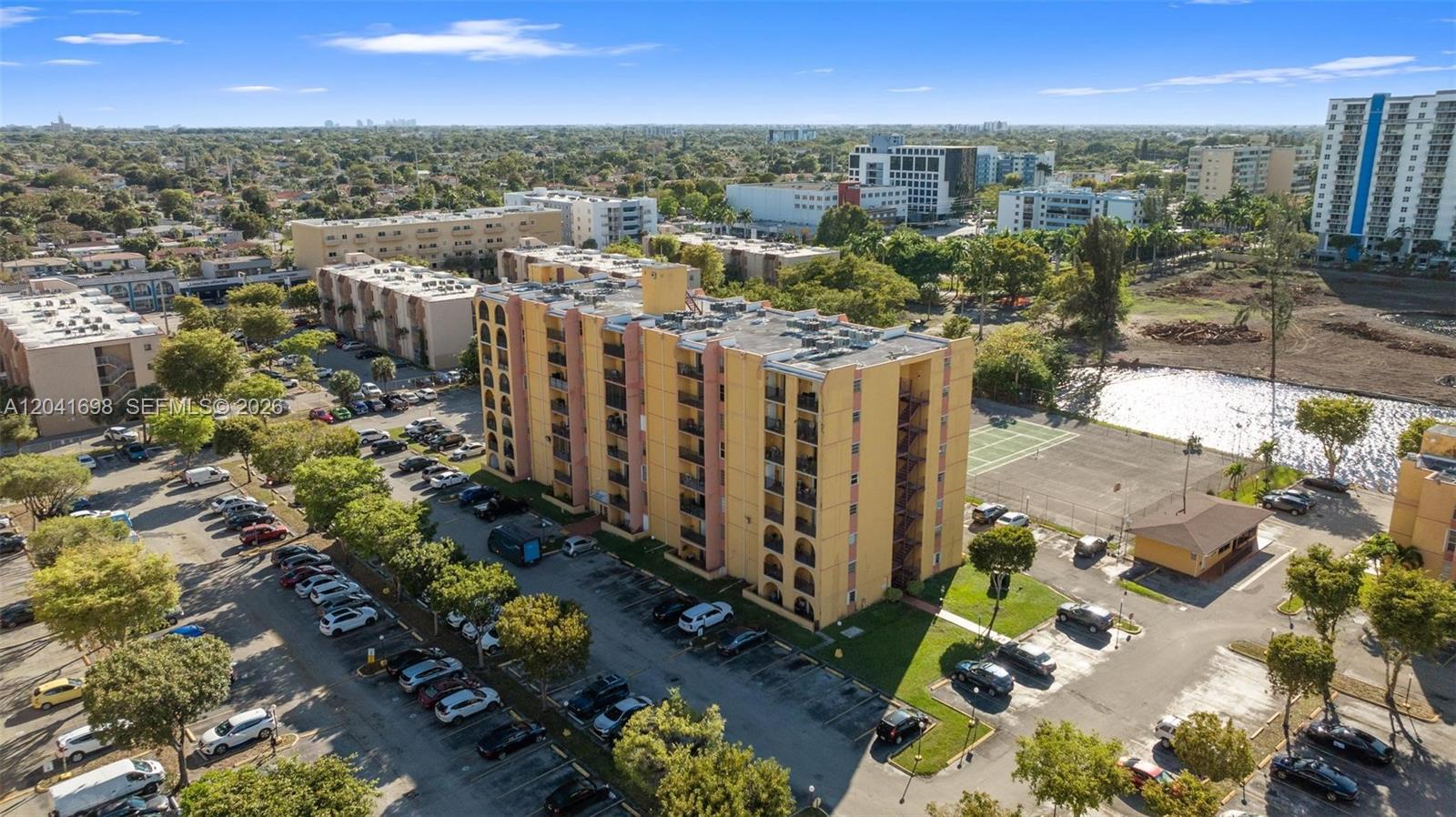 An aerial view shows a multi-story yellow apartment building with a parking lot and pond — 4801 NW 7th St # 16, Miami FL 33126, MIAMI, FL