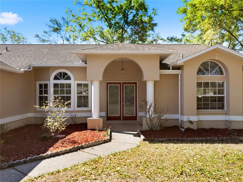 A tan single-story house features a covered entryway with white columns and arched windows — 10358 IRELAND STREET, SPRING HILL, FL