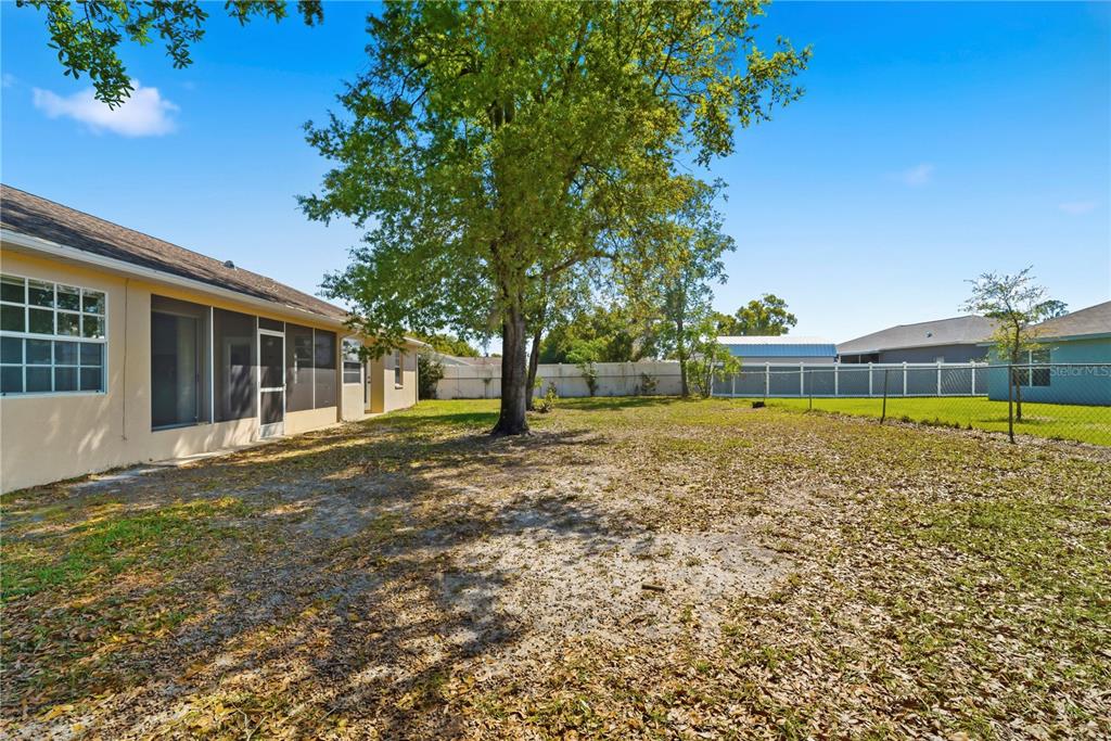 A backyard with a large tree, a screened-in porch, and a white vinyl fence — 10358 IRELAND STREET, SPRING HILL, FL