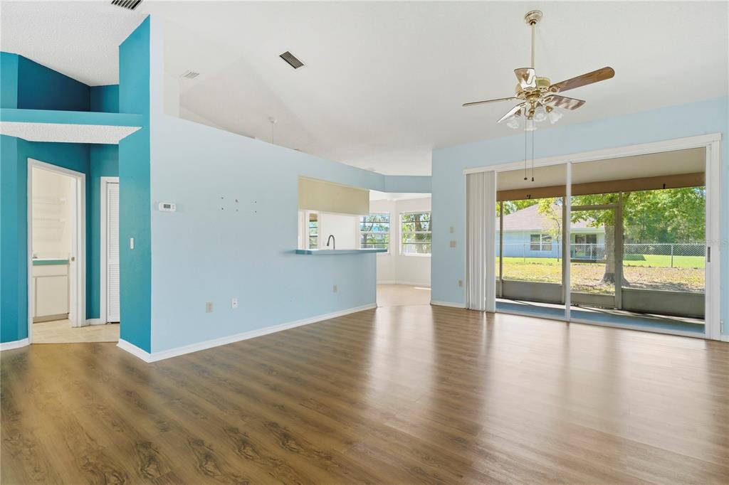 A living room with light blue walls, wood-look flooring, a ceiling fan, and sliding glass doors — 10358 IRELAND STREET, SPRING HILL, FL