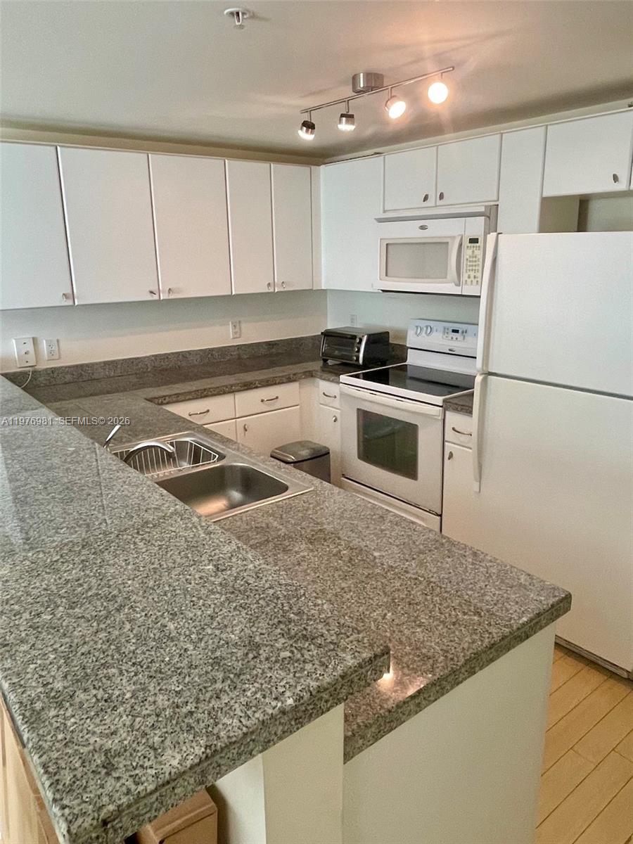A kitchen features white cabinets, granite countertops, and white appliances — 2740 SW 28th Ter # 304, Miami FL 33133, MIAMI, FL