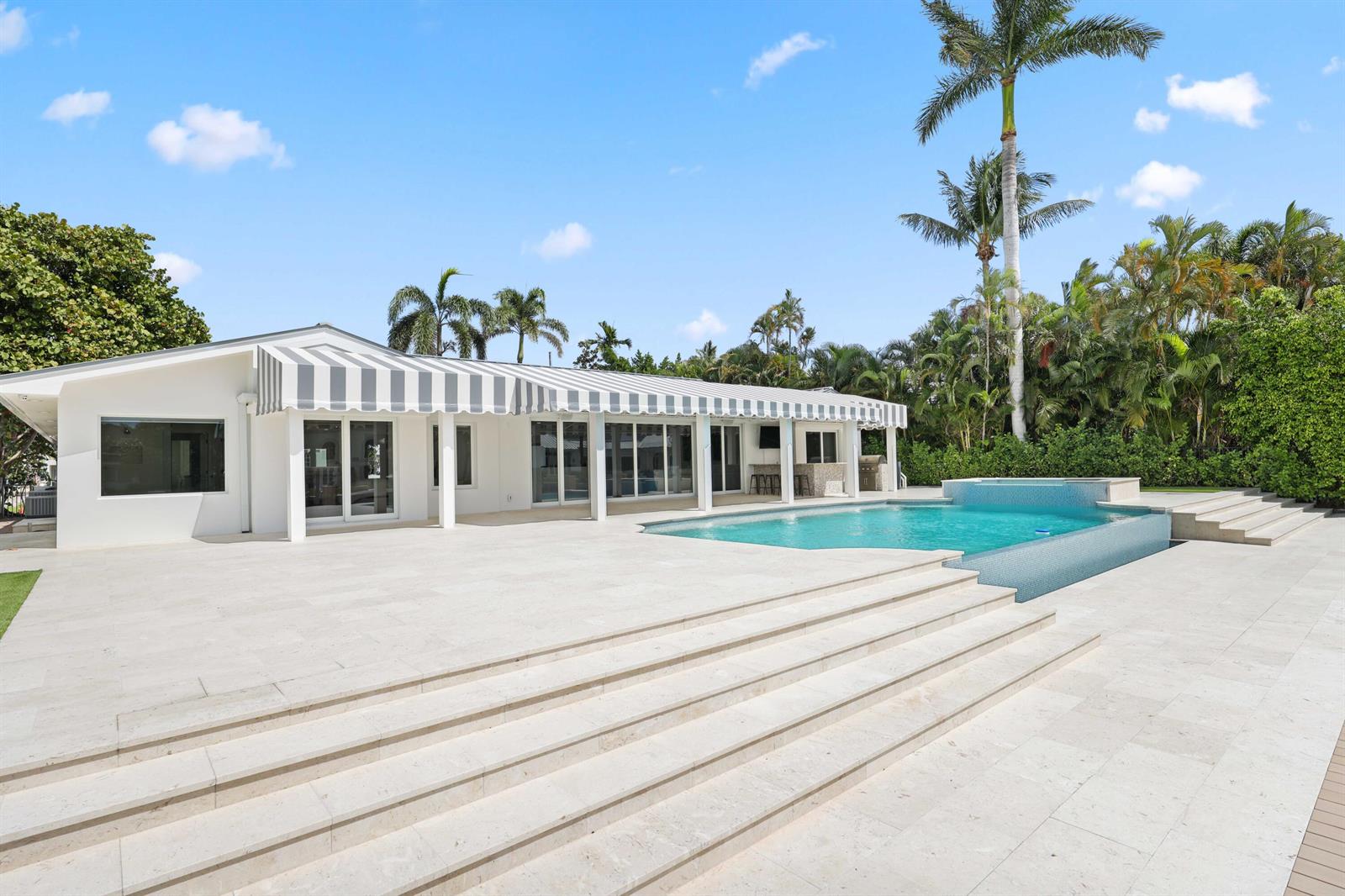 A white house with a striped awning overlooks a swimming pool and stone patio — 1102 Island Drive, Delray Beach FL 33483, DELRAY BEACH, FL