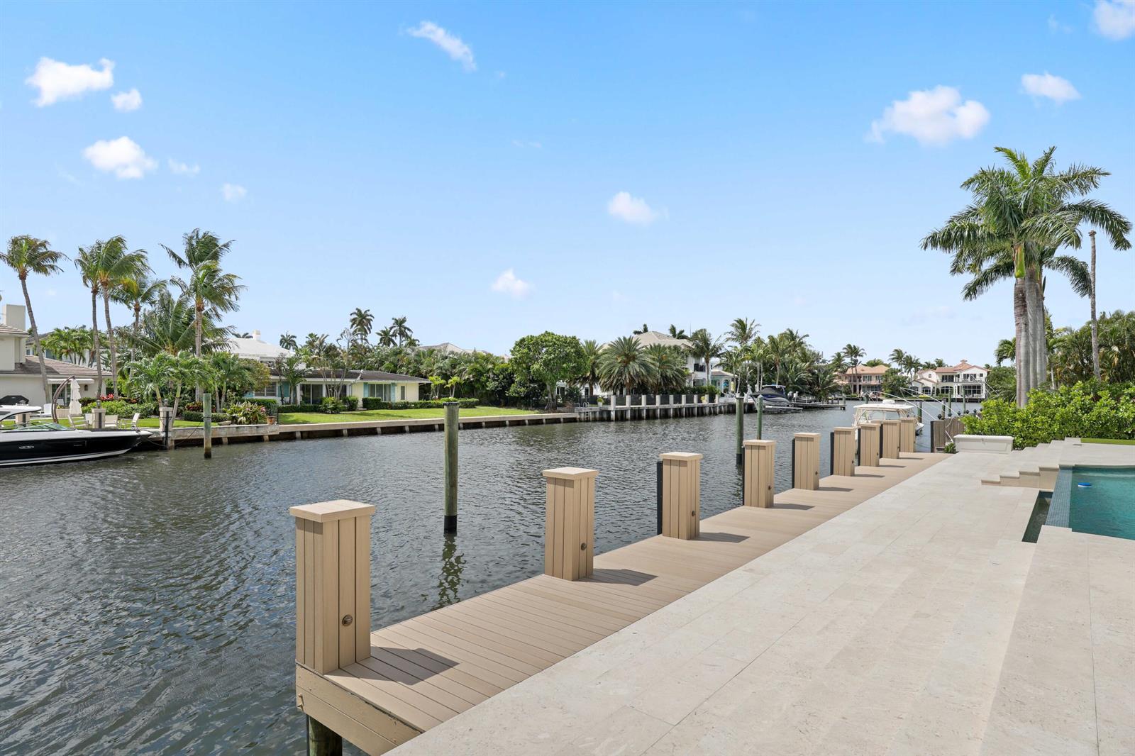 A wooden dock extends into a canal alongside a stone patio and swimming pool — 1102 Island Drive, Delray Beach FL 33483, DELRAY BEACH, FL