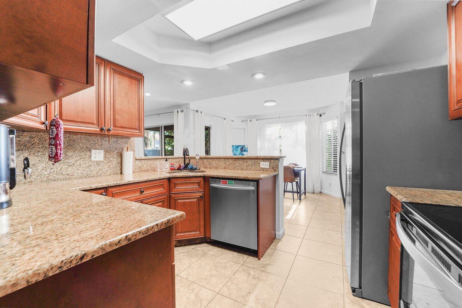 A kitchen with wood cabinets, granite countertops, and a stainless steel dishwasher overlooks a dining area — 6750 Boca Pines Trail # D, Boca Raton FL 33433, BOCA RATON, FL