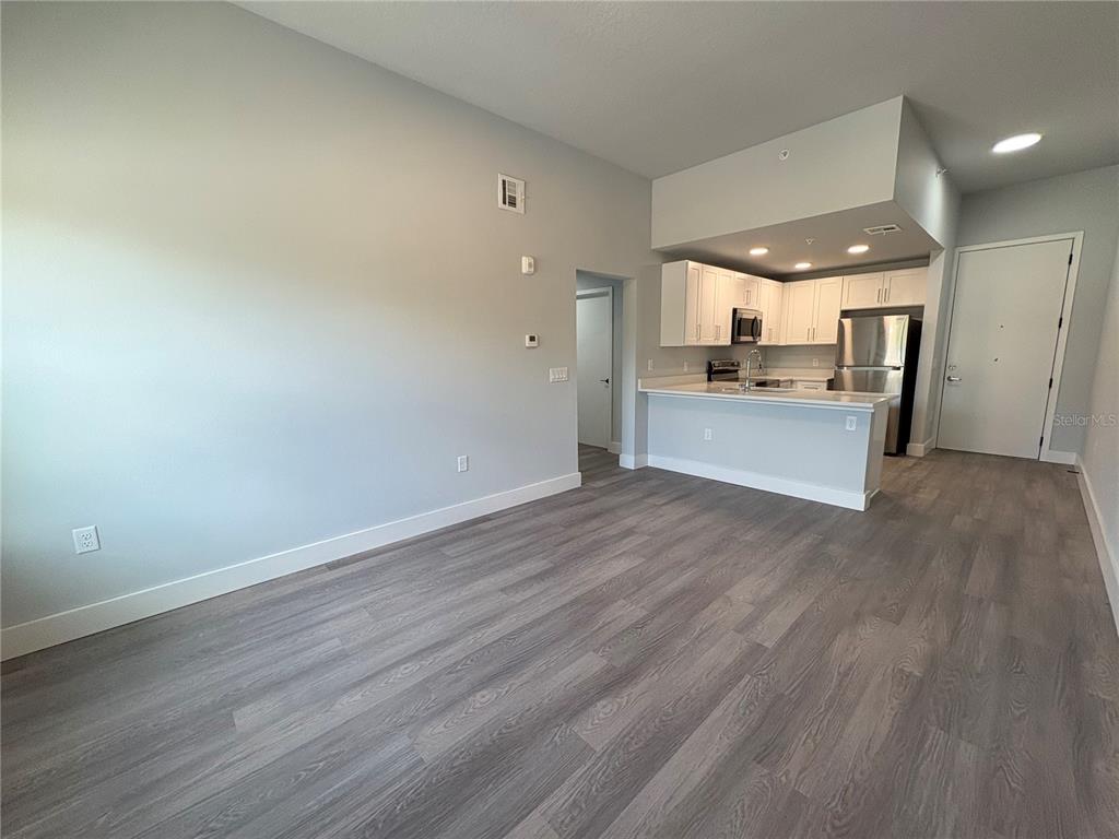 An open-concept living area features light gray walls, wood-look flooring, and an adjacent kitchen — 2240 FLORIDA DRIVE UNIT 101, DELTONA, FL