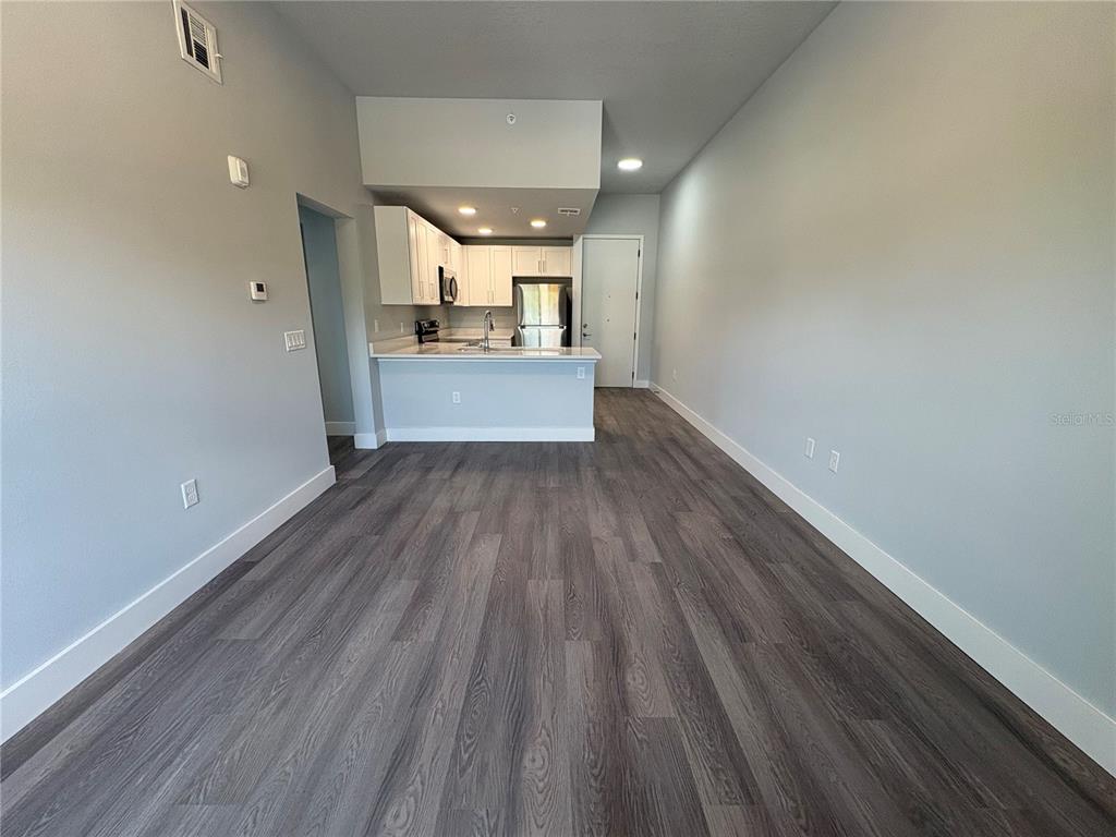 An open-concept living area features gray wood-look flooring and a kitchen with white cabinets — 2240 FLORIDA DRIVE UNIT 101, DELTONA, FL
