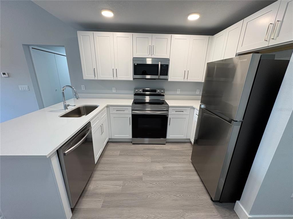 A modern kitchen features white cabinets, stainless steel appliances, and light wood-look flooring — 2240 FLORIDA DRIVE UNIT 101, DELTONA, FL