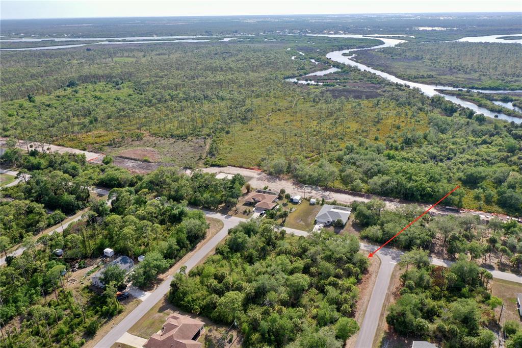 An aerial view shows a vacant, wooded residential lot adjacent to a paved road — 12023 LEROY AVENUE, PORT CHARLOTTE, FL