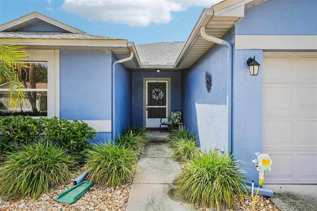A blue house exterior features a concrete walkway leading to a front door with a wreath — 1925 GRAND CYPRESS LANE, SUN CITY CENTER, FL