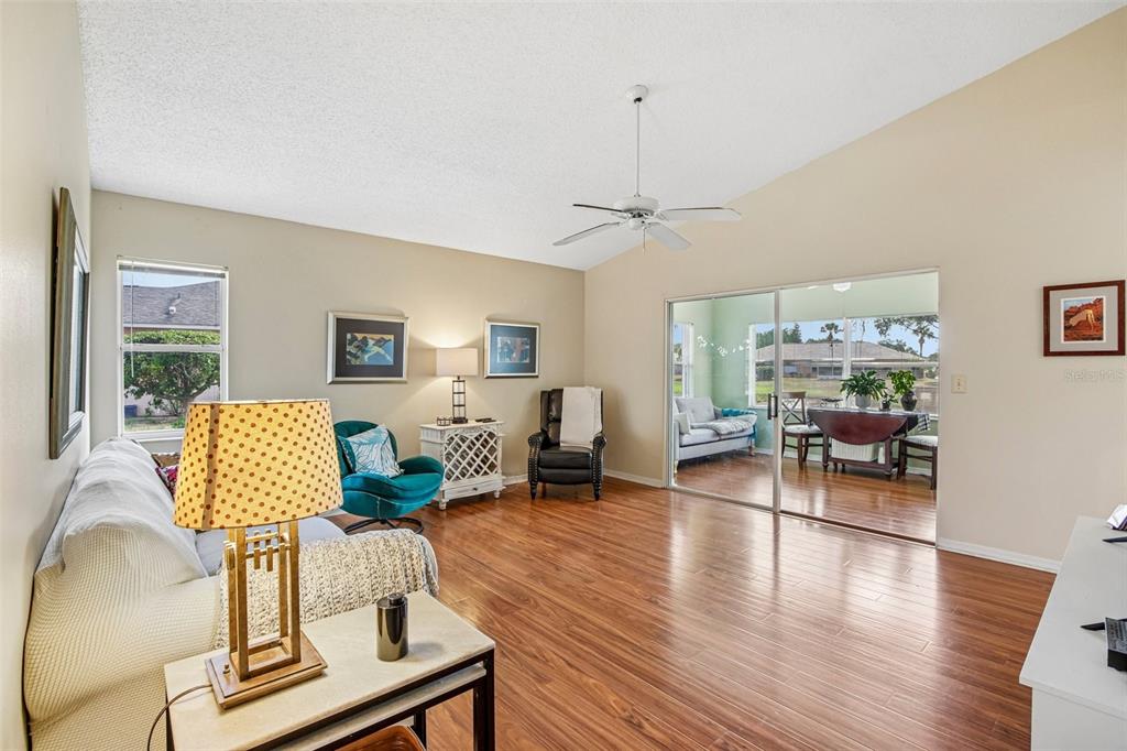 A living room with wood-look flooring, a vaulted ceiling, and sliding doors to a sunroom — 1925 GRAND CYPRESS LANE, SUN CITY CENTER, FL