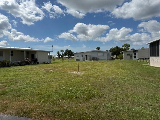 A vacant grassy lot sits between two manufactured homes under a cloudy blue sky — 224 LA ROSAS, NORTH PORT, FL