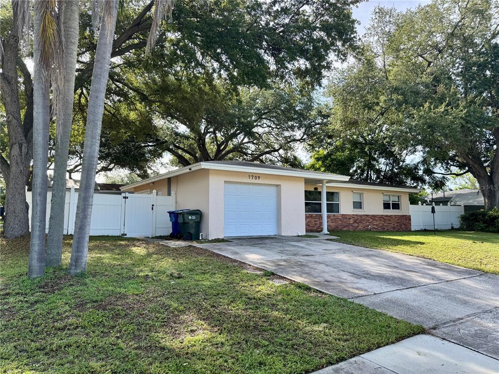 A single-story house with a white garage, brick accents, and a white vinyl privacy fence — 1709 EATON DRIVE NE, CLEARWATER, FL