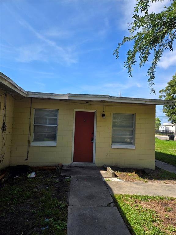 The exterior of a yellow concrete block building features a red door and two windows — 2109 S MILLS AVENUE, ORLANDO, FL