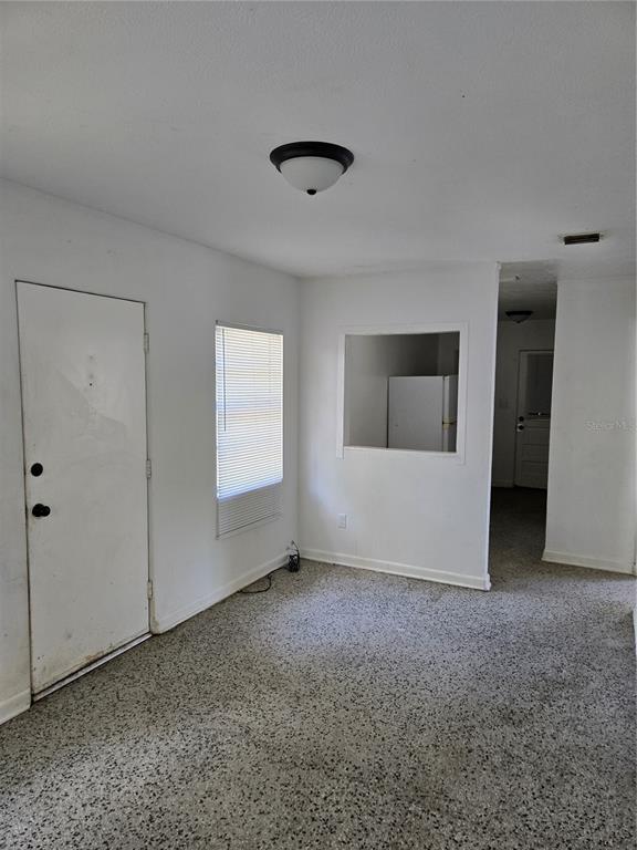 A room with speckled flooring, a white door, a window with blinds, and a pass-through opening — 2109 S MILLS AVENUE, ORLANDO, FL