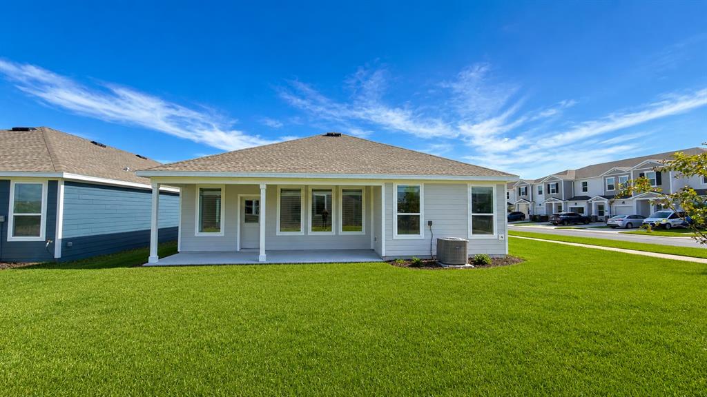 The rear exterior of a single-story house features a covered patio and a grassy yard — 2998 GOOD VIBES WAY, CLERMONT, FL