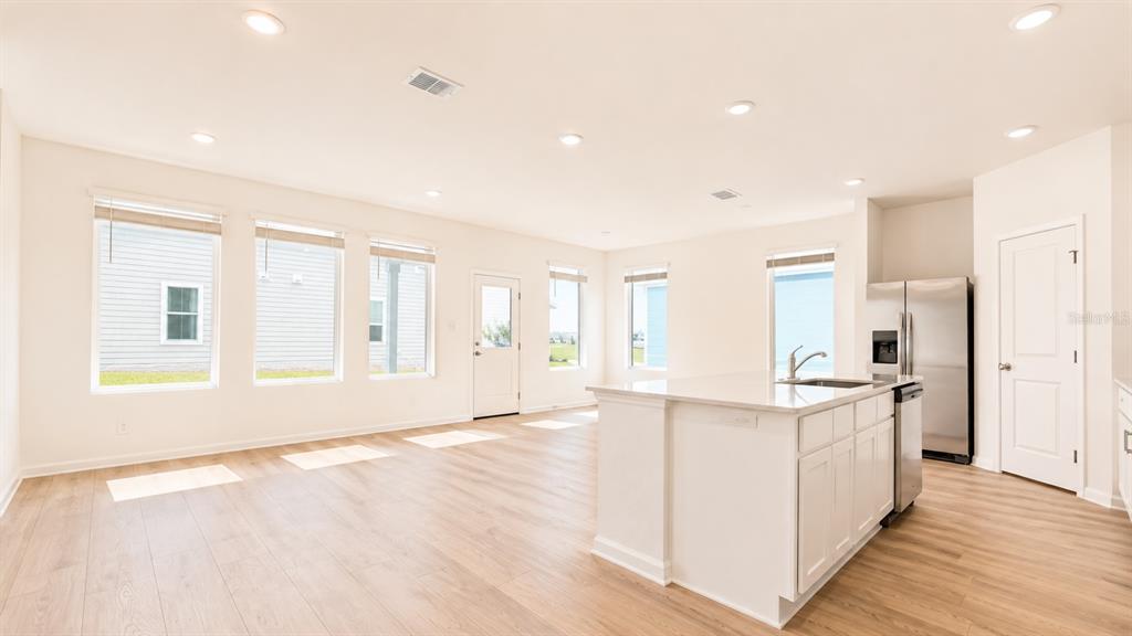 A bright kitchen and living area with light wood floors, white cabinets, and large windows — 2998 GOOD VIBES WAY, CLERMONT, FL