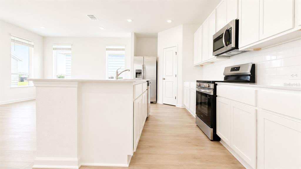 A long hallway with light wood-look flooring, white walls, and two closed white doors — 2998 GOOD VIBES WAY, CLERMONT, FL