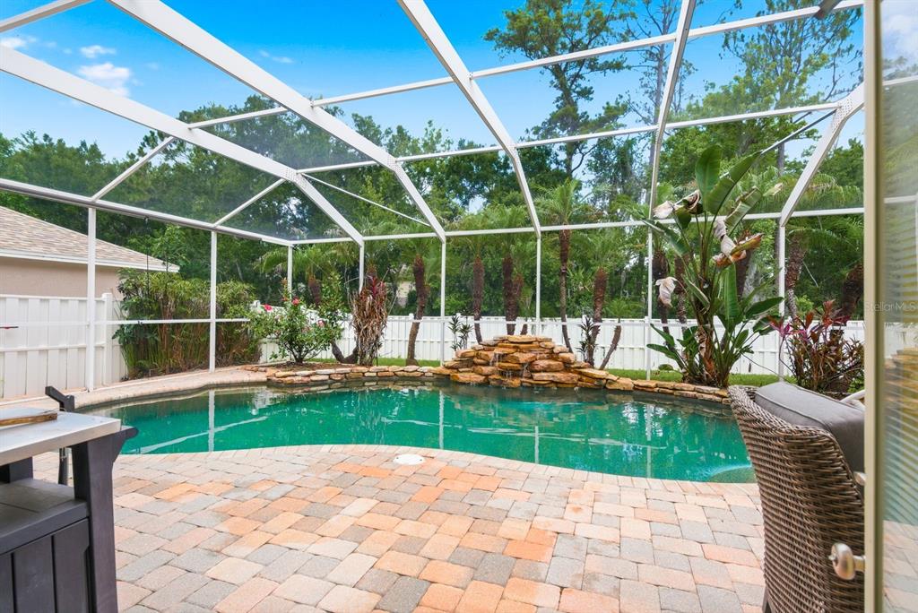 A screened-in patio features a freeform swimming pool with a stone waterfall and brick pavers — 384 WINGATE CIRCLE, OLDSMAR, FL