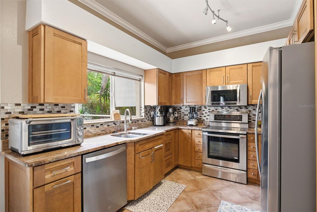 A kitchen features light wood cabinets, stainless steel appliances, granite countertops, and tile flooring — 384 WINGATE CIRCLE, OLDSMAR, FL