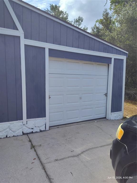 A blue wooden garage with a white sectional door and a concrete driveway — 140 BAY ROAD, OCKLAWAHA, FL