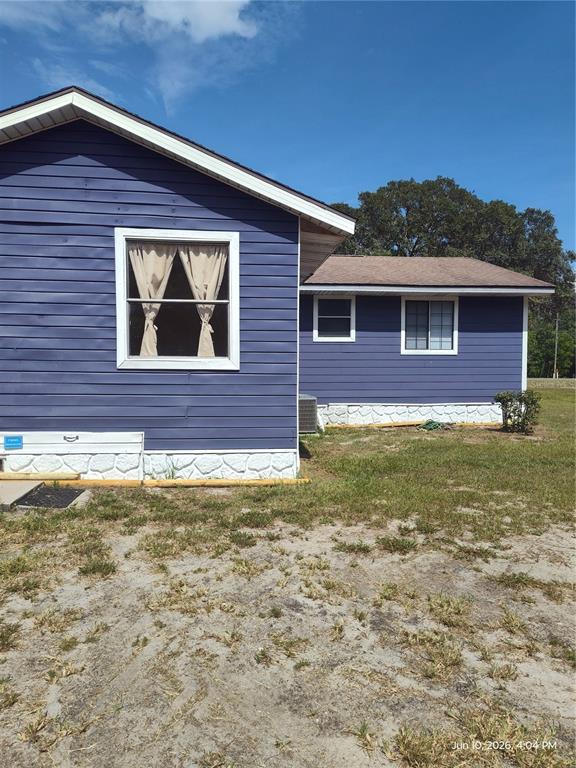 The exterior of a blue house features white stone skirting and two windows — 140 BAY ROAD, OCKLAWAHA, FL
