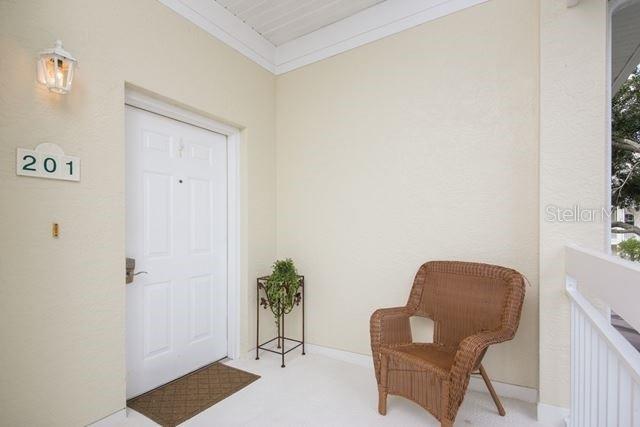 A white front door with a wicker chair on a small covered balcony — 3706 54TH DRIVE W UNIT 201, BRADENTON, FL