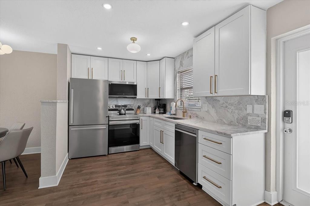 A kitchen features white cabinets, stainless steel appliances, and marble-look countertops and backsplash — 5830 MIDNIGHT PASS ROAD UNIT 43, SARASOTA, FL