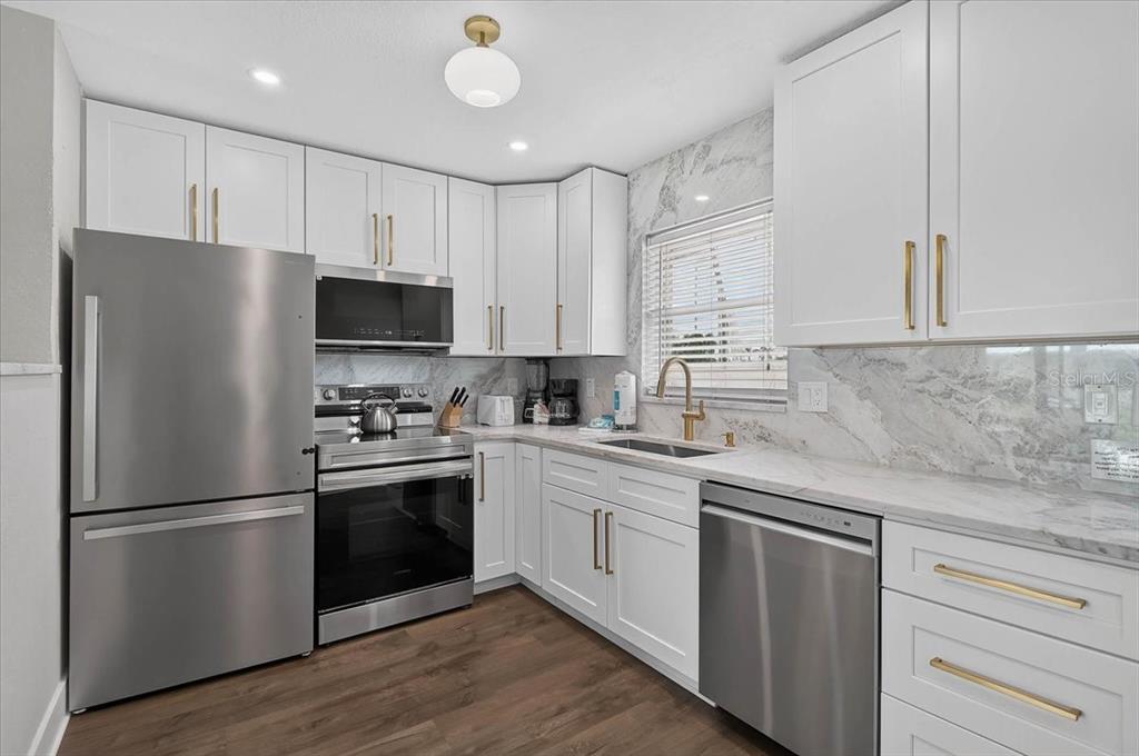 A kitchen features white cabinets, stainless steel appliances, marble-look countertops, and dark wood flooring — 5830 MIDNIGHT PASS ROAD UNIT 43, SARASOTA, FL