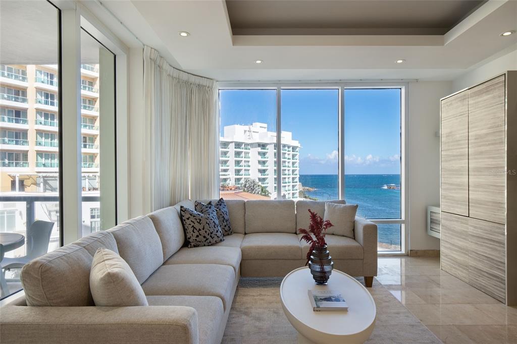 A living room features a sectional sofa, a coffee table, and floor-to-ceiling windows overlooking the ocean — 5 AVE MUNOZ RIVERA UNIT 404, SAN JUAN, PR