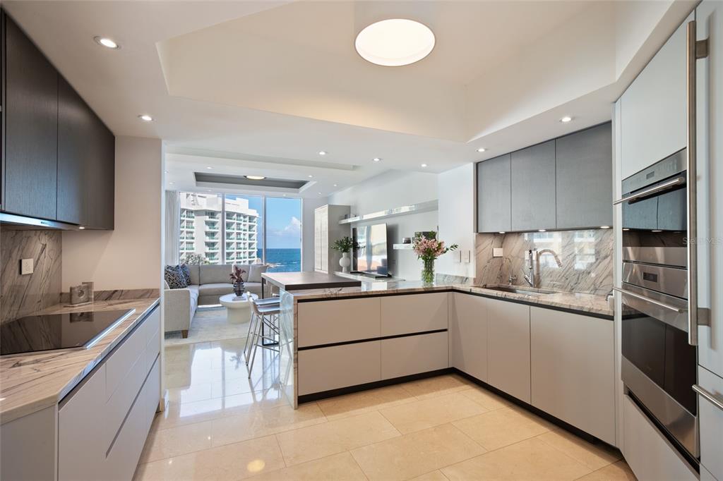 A modern kitchen with light gray cabinets and marble countertops opens to a living area — 5 AVE MUNOZ RIVERA UNIT 404, SAN JUAN, PR