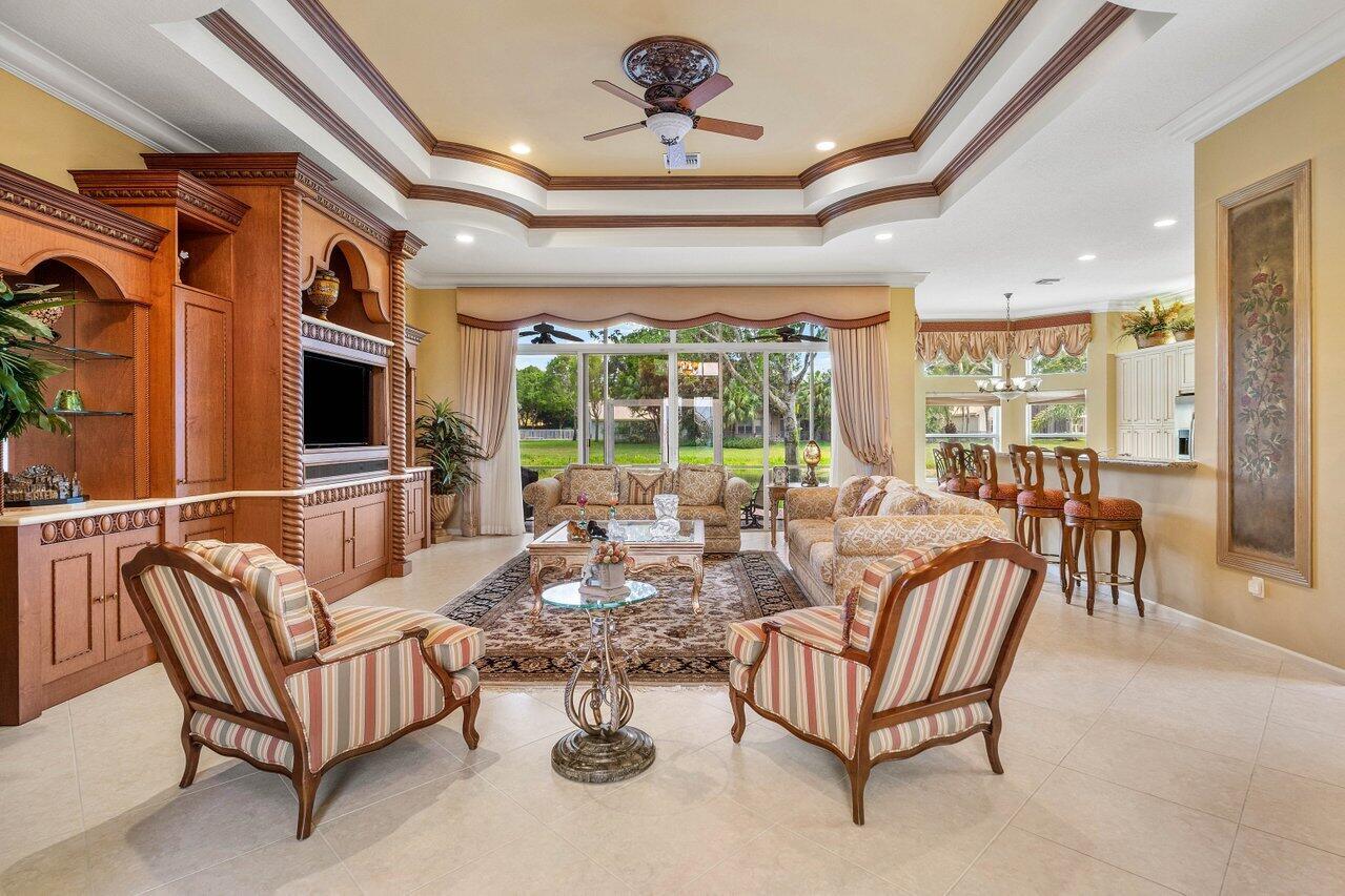 A spacious living room features a tray ceiling, built-in cabinetry, and a view of greenery — 6558 Sand City Way, Delray Beach FL 33446, DELRAY BEACH, FL