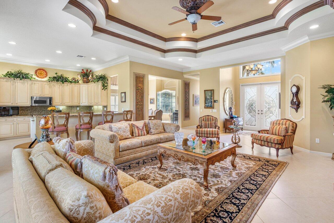 A spacious living room with a tray ceiling, beige furniture, and an open-concept kitchen — 6558 Sand City Way, Delray Beach FL 33446, DELRAY BEACH, FL