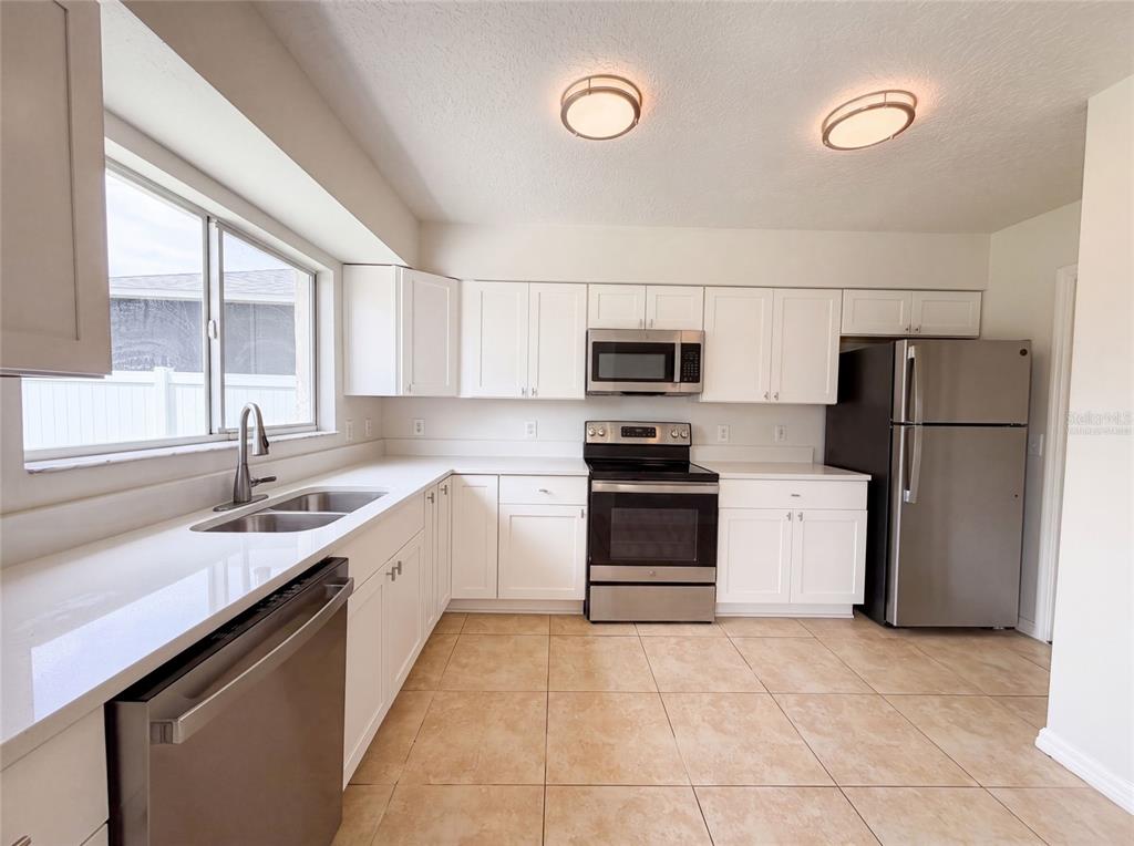 A kitchen features white cabinets, stainless steel appliances, white countertops, and light-colored tile flooring — 13236 PIKE LAKE DRIVE, RIVERVIEW, FL