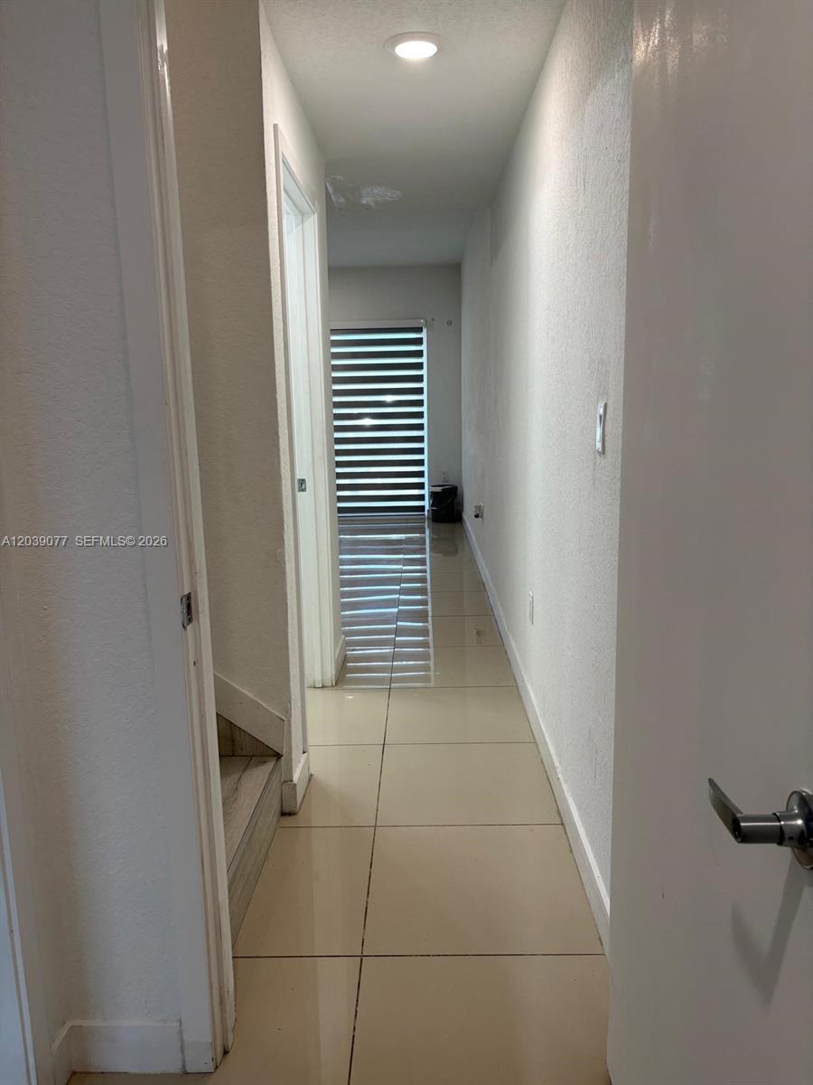 A narrow hallway with light-colored tile flooring leads toward a window with striped blinds — 25680 SW 143rd Path, Homestead FL 33032, HOMESTEAD, FL