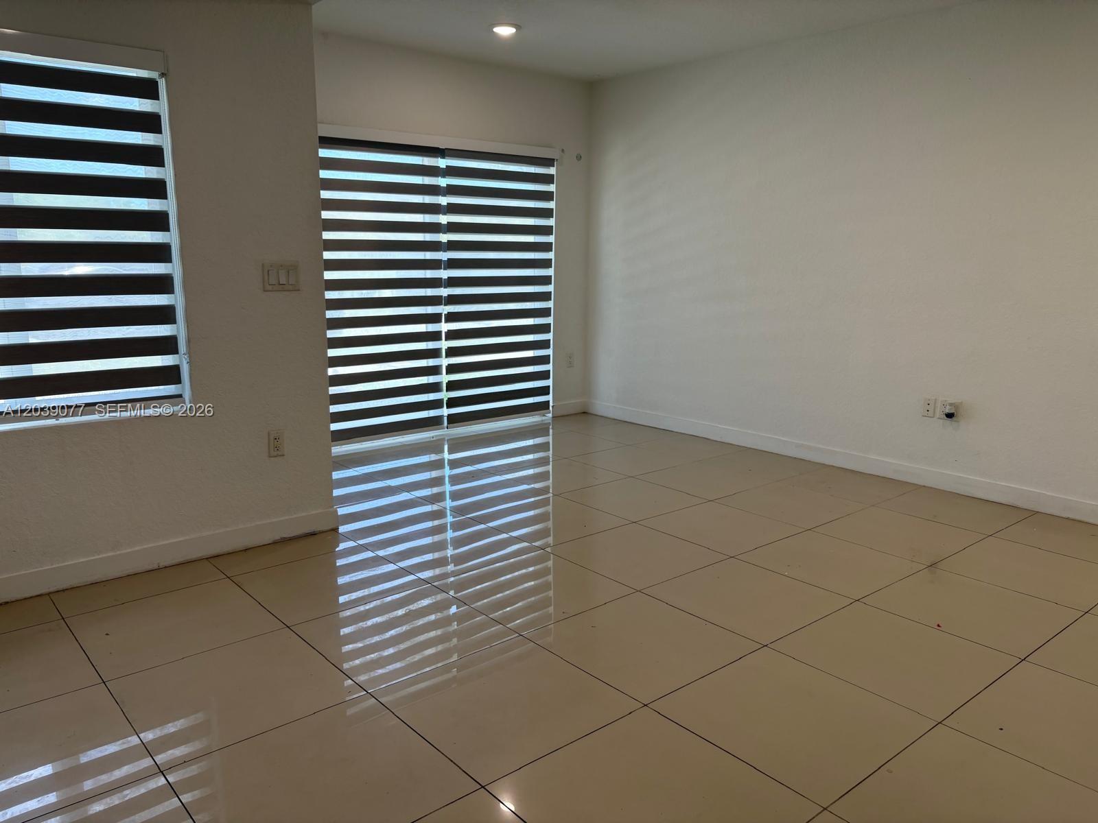 An empty room features beige tile flooring, white walls, and horizontal window blinds — 25680 SW 143rd Path, Homestead FL 33032, HOMESTEAD, FL