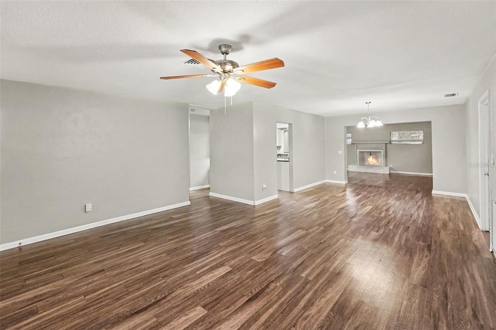 An open-concept living area features wood-look flooring, a ceiling fan, and a distant fireplace — 2098 62ND TERRACE S, ST PETERSBURG, FL