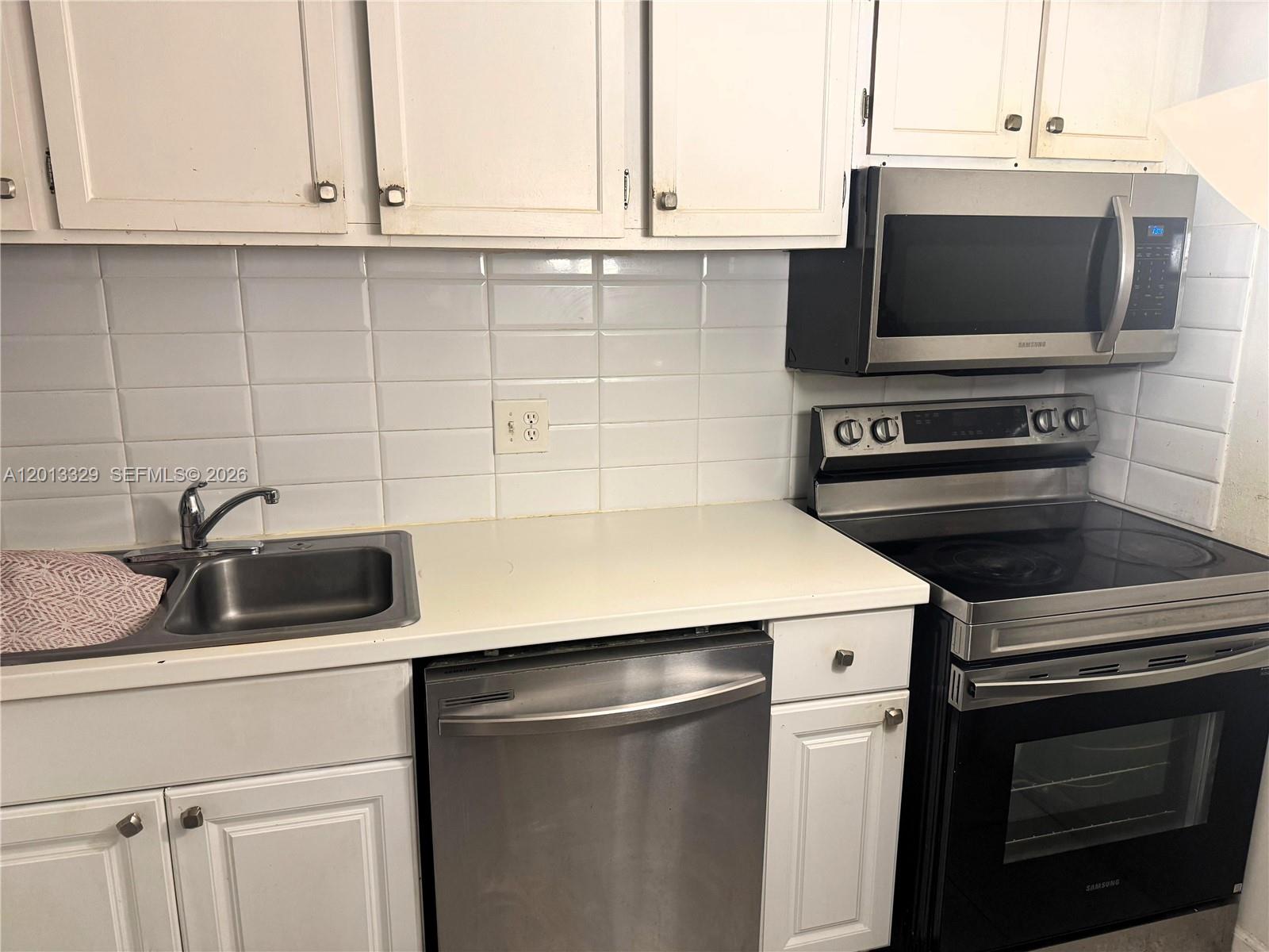 A kitchen features white cabinets, stainless steel appliances, a sink, and a white tiled backsplash — 3740 Inverrary Dr # 2B, Lauderhill FL 33319, LAUDERHILL, FL
