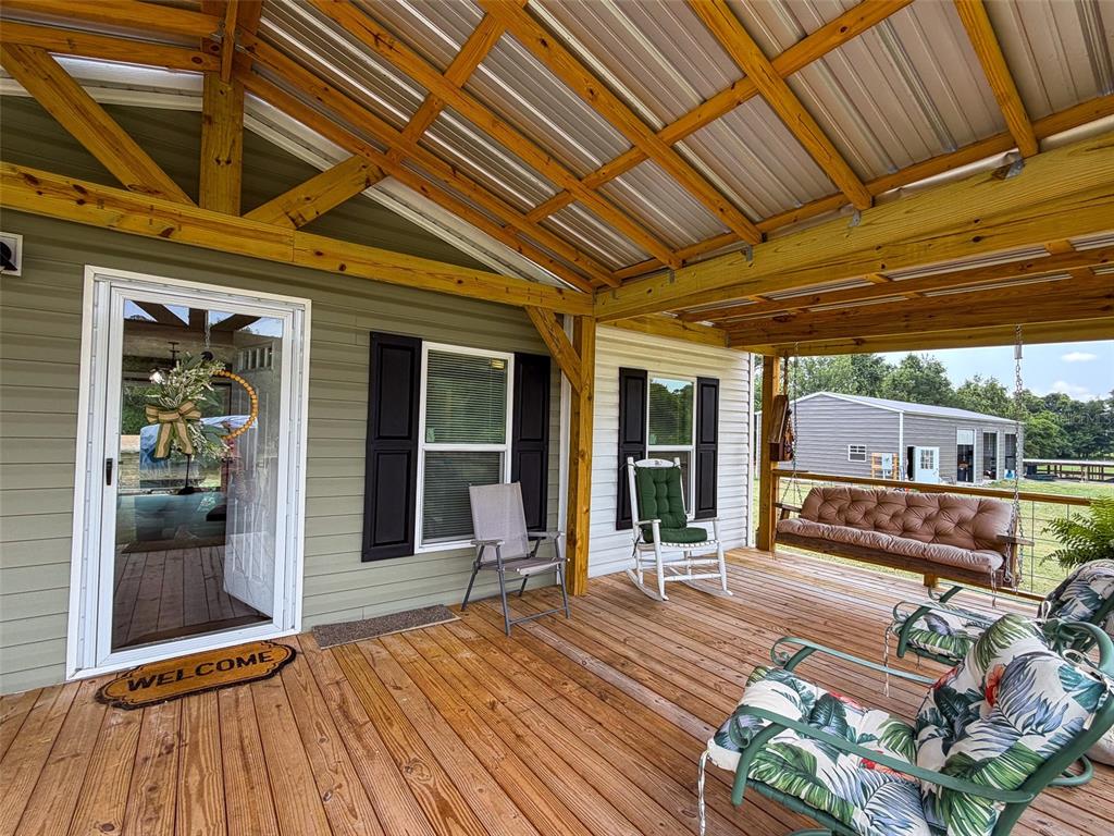 A covered wooden porch features a swing, rocking chairs, and a glass-paneled front door — 330 SW CHALET TERRACE, FORT WHITE, FL