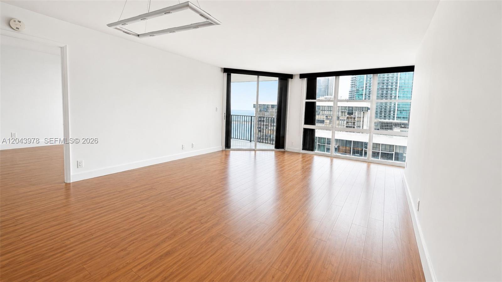 An empty room features wood-look flooring, white walls, a modern light fixture, and floor-to-ceiling windows — 1901 Brickell Av # B2203, Miami FL 33129, MIAMI, FL
