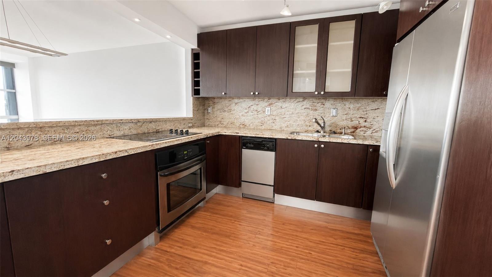 A kitchen features dark wood cabinetry, granite countertops, and stainless steel appliances — 1901 Brickell Av # B2203, Miami FL 33129, MIAMI, FL