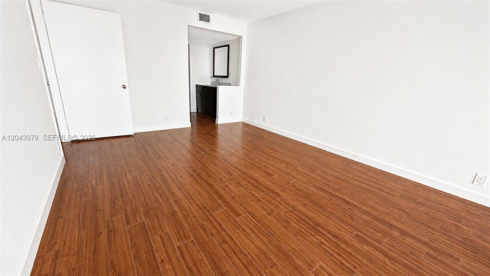 An empty room with wood-look flooring and a doorway leading to a bathroom vanity — 1901 Brickell Av # B2203, Miami FL 33129, MIAMI, FL