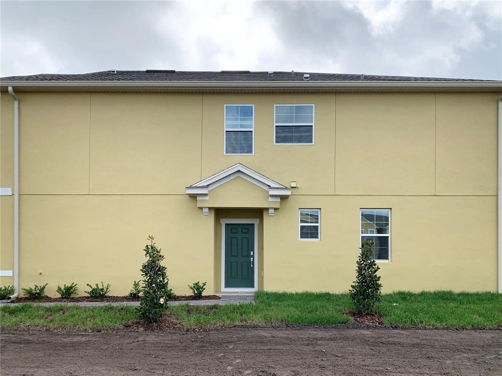 A two-story yellow stucco townhouse exterior with a dark green front door and landscaping — 9963 RED EAGLE DRIVE, ORLANDO, FL
