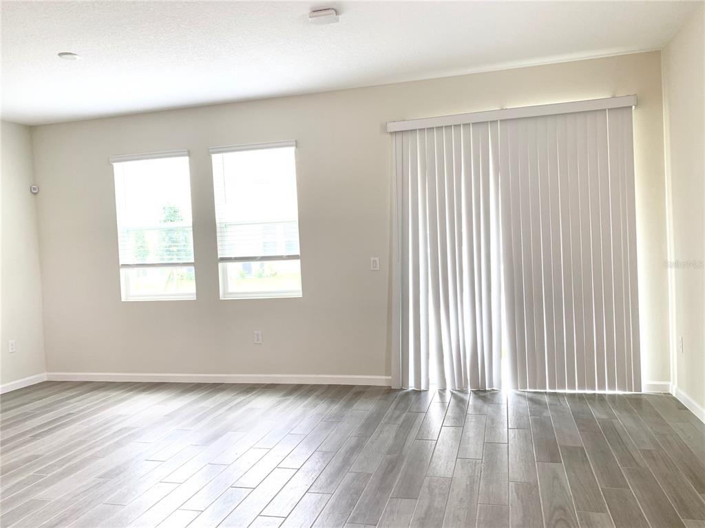 An empty living room features light-colored walls, gray wood-look flooring, two windows, and sliding doors — 9963 RED EAGLE DRIVE, ORLANDO, FL