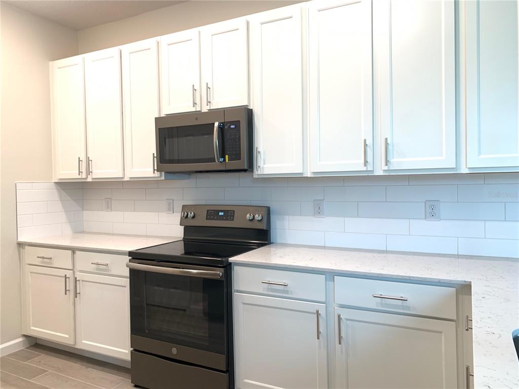 A kitchen features white cabinets, a dark microwave and stove, and a white subway tile backsplash — 9963 RED EAGLE DRIVE, ORLANDO, FL