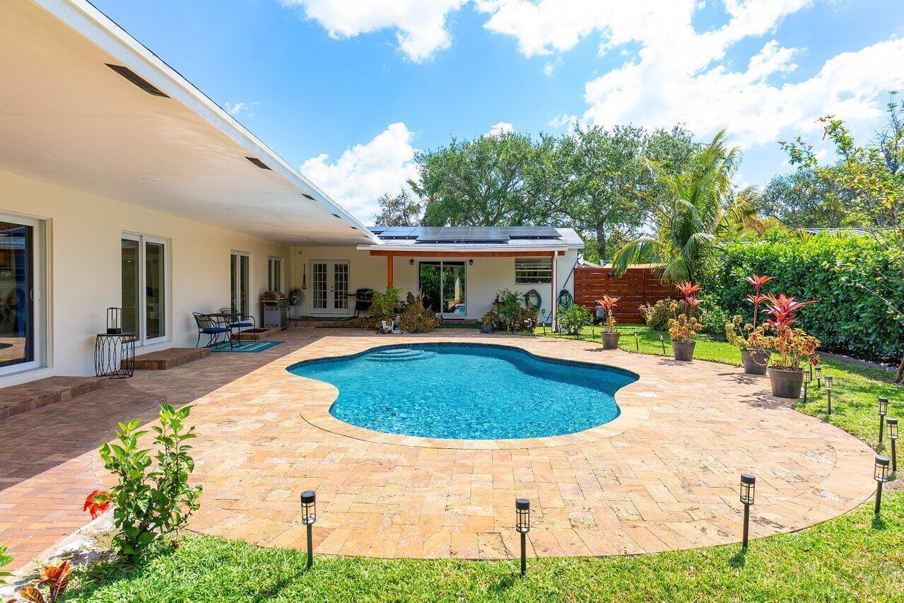 A backyard features a kidney-shaped swimming pool surrounded by a stone patio and landscaping — 1650 NE 3rd Avenue, Delray Beach FL 33444, DELRAY BEACH, FL