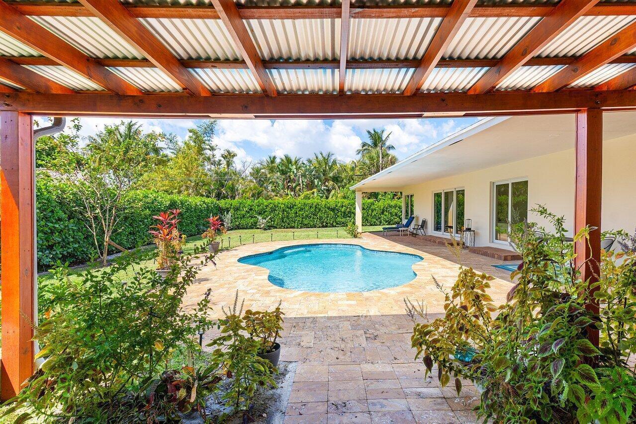 A backyard patio with a wooden pergola overlooks a swimming pool and a landscaped lawn — 1650 NE 3rd Avenue, Delray Beach FL 33444, DELRAY BEACH, FL