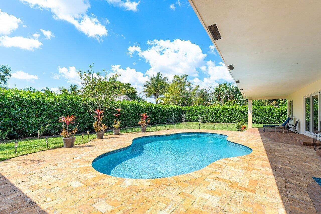 A backyard features a kidney-shaped swimming pool, a stone patio, and a covered porch — 1650 NE 3rd Avenue, Delray Beach FL 33444, DELRAY BEACH, FL