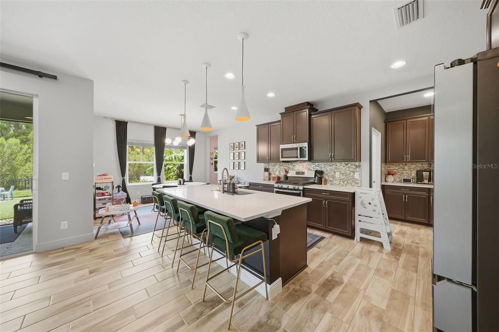 A kitchen features dark wood cabinets, a white quartz island with green stools, and tile flooring — 4801 BALLANTRAE BOULEVARD, LAND O LAKES, FL